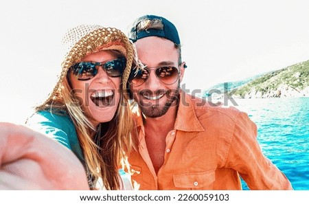 Young happy couple in love taking selfie at sailboat excursion with water camera - Boat trip life style in exotic scenarios - Youth lifestyle and travel concept around the world - Warm bright filter