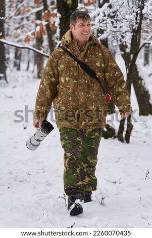 Professional wildlife photographer in a snowy oak forest with his telephoto lens on camera