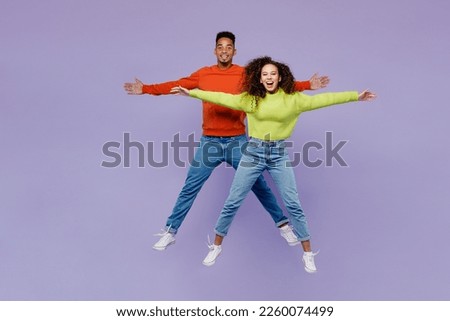 Full body young couple two friends family man woman of African American ethnicity wear casual clothes together jump high with outstretched hands arms isolated on pastel plain light purple background