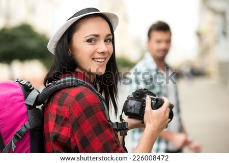 Woman is taking picture of boyfriend on tourist journey. She is looking at the camera.