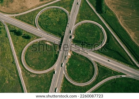 Clover or daisy type of road junction. Aerial top down view of beautiful highway road junction in clover shape at summer day. Lorry truck and semi-truck on highway. Logistic concept