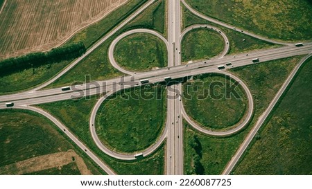 Clover or daisy, simple and cheap type of road junction. Aerial view of beautiful highway road junction in clover shape at summer day. Lorry truck and semi-truck on highway. Car and logistic concept