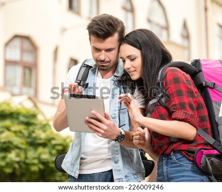 Young tourists are looking at the tablet in the town.
