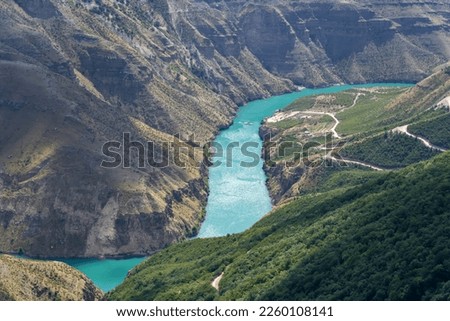 Turquoise river Sulak meandering through rocky forested landscape. Gorge of mountain river with village and boats
