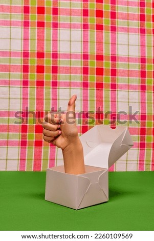 Pop art photography. Female hand sticking out food box and showing gesture of approvement over retro background. Creativity, art. Complementary colors. Copy space for ad, text
