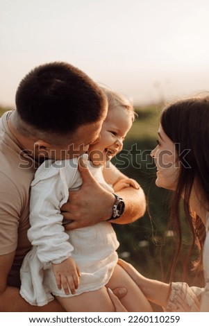 Beautiful caucasian family of father, mother and little daughter posing on camera on background of green field Royalty-Free Stock Photo #2260110259