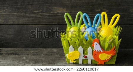 Easter basket with decorative eggs on a wooden background.  Multi-colored rabbits hid in a basket.  Easter holiday.  Copy space for text, foreground.  Children's crafts.