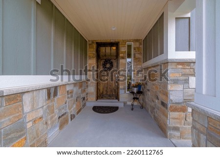 Utah- House with dark wood front door with glass pane and wreath. Home with gray board and batten and stone veneer siding by the entrance to the front door with sidelights and potted flowers. Royalty-Free Stock Photo #2260112765