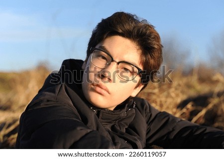 A handsome teenager boy with glasses looking into camera with serious face on a sunny day