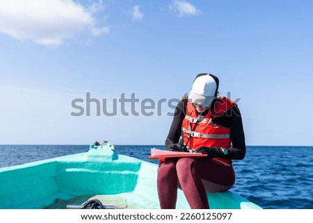 Marine biologist writing down data sitting on top of a boat in the middle of the sea Royalty-Free Stock Photo #2260125097