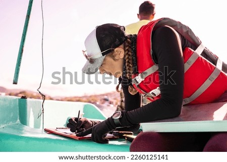 Profile of a marine biologist writing data on top of a boat at sea Royalty-Free Stock Photo #2260125141