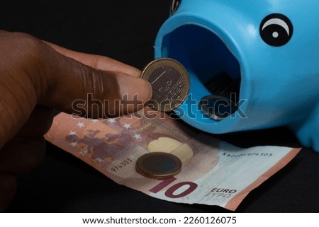 hand holding a one euro coin and putting it in piggy bank