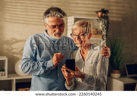 Portrait of a happy senior married couple using smartphone while relaxing at home together. Smiling mature grandparents having fun with mobile phone at home and browsing internet or online shopping. Royalty-Free Stock Photo #2260140245