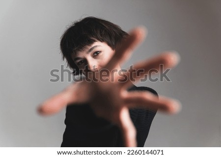Short-haired young woman reaching towards the camera. Blurred hand in the foreground. Focus on the background. High quality photo