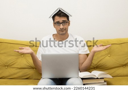 Tired and bored student sitting on the couch with many books and laptop. Online education and preparation for examinations concept