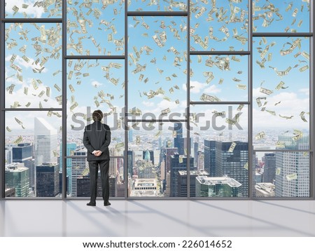 Businessman in a modern office looking at the city and falling dollars