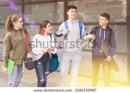 Smiling teenage friends spending time together and talking to each other near college building on a sunny day Royalty-Free Stock Photo #2260150987
