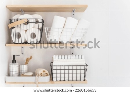 Beautiful white bathroom. Wooden shelves. Rolled towels, stacked towels and baskets. Soap, washcloth, toilet paper and toothbrushes. Indoor flowers. Eco style, minimalism. Royalty-Free Stock Photo #2260156653