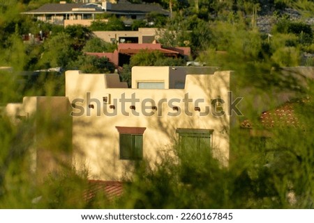 Hidden house facade as seen through plants and trees in a rural part of the city with white stucco exterior home in desert. In late afternoon sun in the hills of arizona and southwestern america.