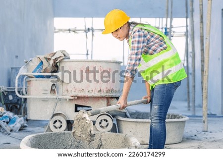 asian woman worker hardworking as a labor staff in construction site work mix concrete cement by hand Royalty-Free Stock Photo #2260174299