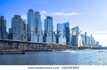 Glimmering steel and glass skyscraper buildings along Henry Hudson Parkway, known as the West Side Highway, Manhattan, New York City, on a sunny winter day. Hudson River in foreground. Skyline, NYC. Royalty-Free Stock Photo #2260183801