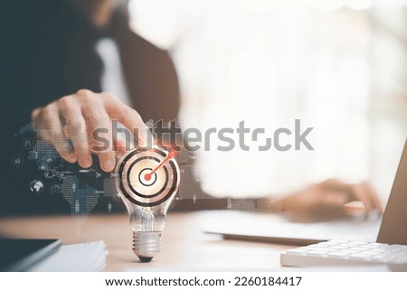 businessman pointing to a light bulb and arrow icon hitting center of dartboard target,Setting business goals and focused concepts, Organizational growth and objectives, marketing strategy planning
