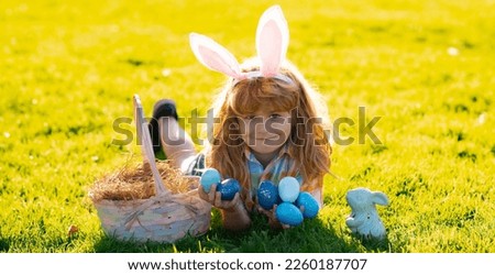 Spring holiday. Kid boy lying on the grass and finding easter eggs. Child boy with easter eggs and bunny ears on grass. Panoramic web banner frame.