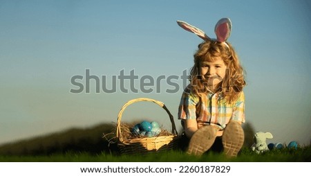 Wide photo banner for website header design. Cute bunny child boy with rabbit ears. Children hunting easter eggs on sky background with copy space.