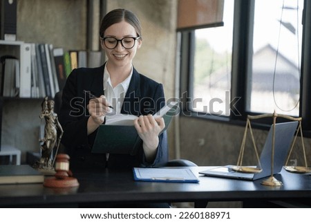 A female lawyer working on a laptop computer and reading law books and taking notes on office work legal service concept.