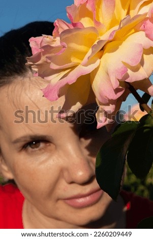 Blurred portrait of a woman looking at the camera in the background and a large light yellow rose in full bloom in the foreground, selective focus.