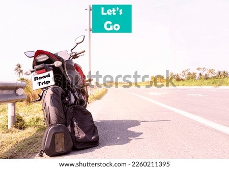Motorcycle parked and black backpack with message Let's go on green roadsign on highway road view