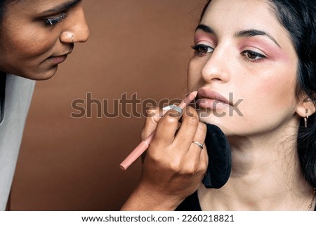 Stock photo of young model in studio having her makeup done by professional artist.