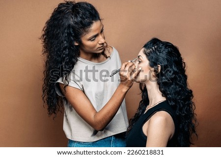 Stock photo of beautiful young woman doing makeup to her client in studio.