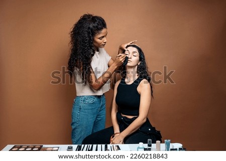 Stock photo of cool makeup artist doing makeup to her client in studio. She is doing her eyeliner.