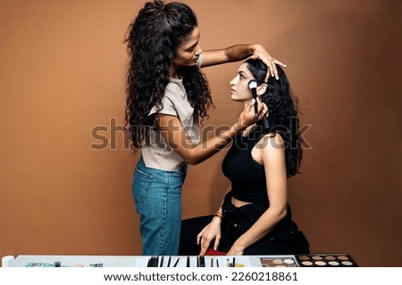 Stock photo of latin make up artist using brush and colorful eyes shadow with her friend in studio.