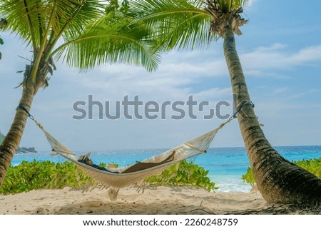 women in a hammock under a palm tree at Petite Anse beach Mahe Tropical Seychelles Islands. Royalty-Free Stock Photo #2260248759
