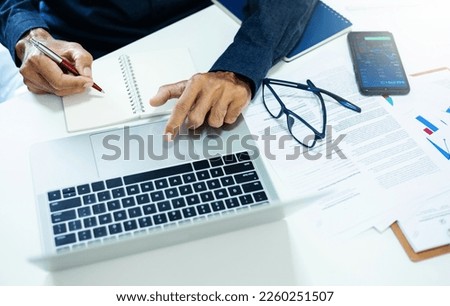 Asian businessmen working on computer laptop and write on notepad with to calculate financial statements and analysis chart on mobile and paper chart, top view photo