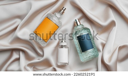 Luxury bottles of perfume on beige silk, flat lay