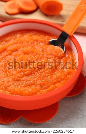 Healthy baby food. Bowl with delicious carrot puree on light grey marble table, closeup
