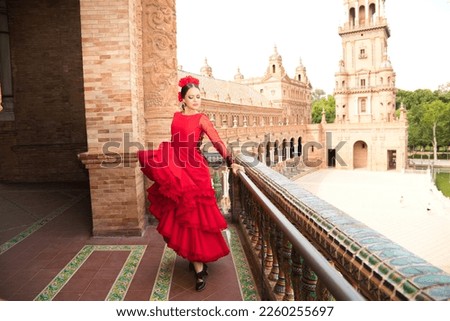 Beautiful teenage woman dancing flamenco on the balcony of a square in Seville. She wears a red dress with ruffles with a lot of art. Flamenco cultural heritage of humanity. Royalty-Free Stock Photo #2260255697