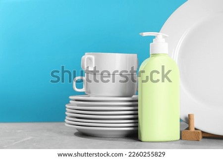 Set of clean tableware and dish detergent on grey table against light blue background. Space for text