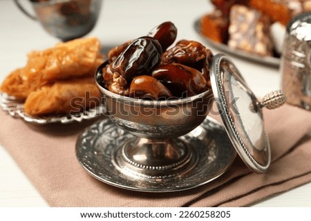 Date fruits, Turkish delight and baklava dessert served in vintage tea set on white wooden table, closeup