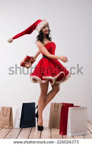 Woman shopping for christmas gifts. Young caucasian girl dancing with shopping bags wearing Santa Claus dress and hat