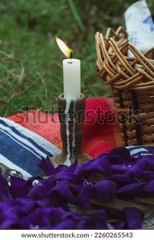 Close up burning candle in wooden holder beside picnic woven basket concept photo. Front view photography with blurred background. High quality picture for wallpaper, travel blog, magazine, article