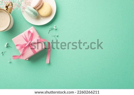 Spring presents concept. Top view photo of pink giftbox with ribbon bow plate with macarons cup of coffee and gypsophila flowers on isolated teal background with empty space