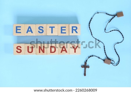 Easter Sunday holy week concept. Wooden blocks typography with rosary flat lay in blue background.