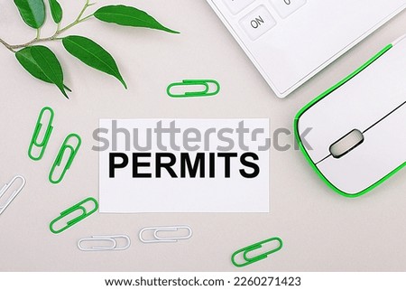 On a light background, a white calculator, a computer mouse, green paper clips, a green plant and a white blank sheet with the text PERMITS. Flat lay.