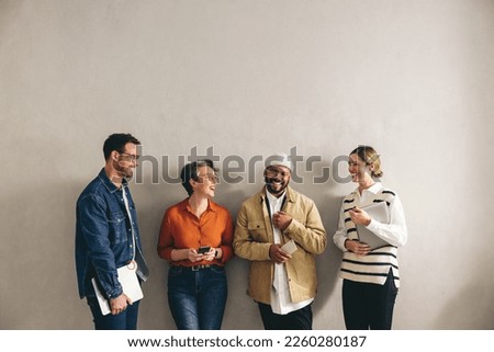 Happy businesspeople smiling cheerfully while waiting in line for an interview. Group of shortlisted job candidates holding different digital devices in a modern workplace. Royalty-Free Stock Photo #2260280187