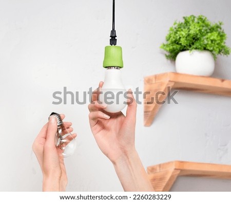 female hands screw in an energy-saving LED light bulb Royalty-Free Stock Photo #2260283229