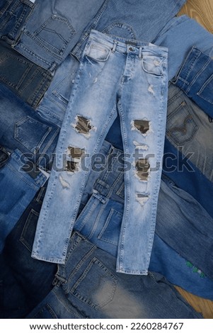 Closeup torn jeans with Lots of jeans pants in a stack. Denim background